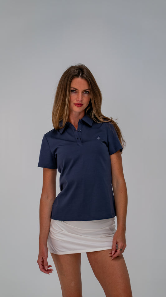Model wearing Le Classique Polo Women in navy with a white skirt, front view