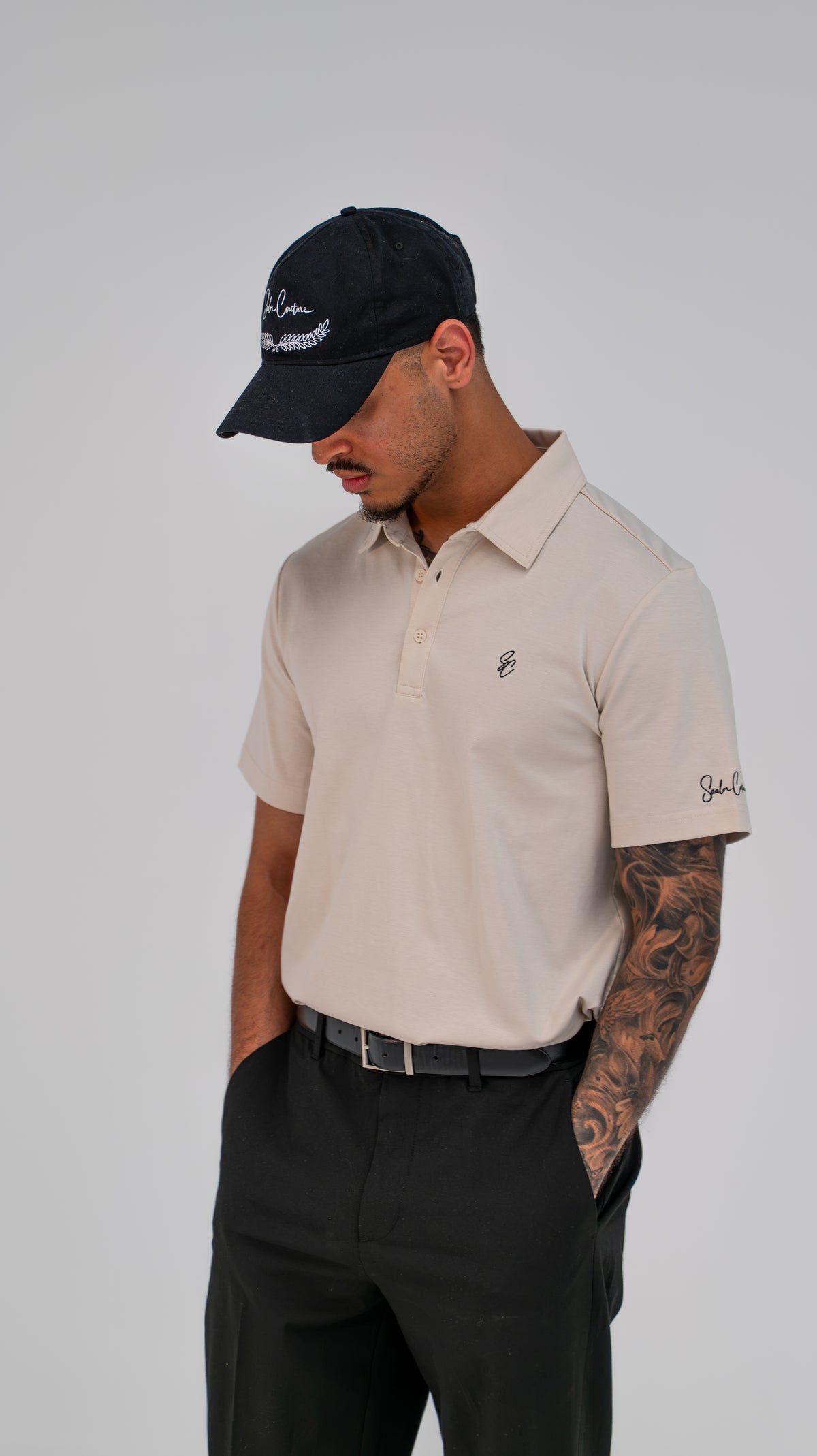 Model wearing Le Classique Polo in cream with black trousers and a Saalor Couture cap