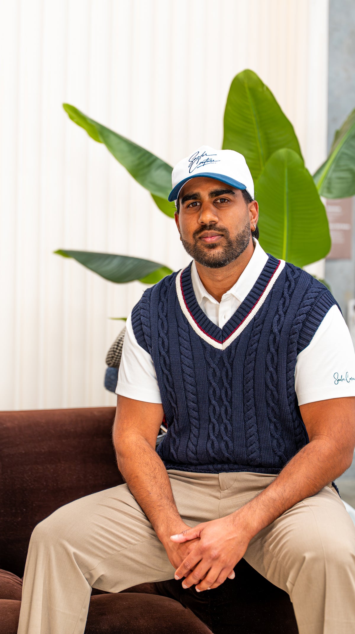 Golfer seated in a navy cable-knit vest over a white Saalor Couture polo, with a Saalor Couture cap